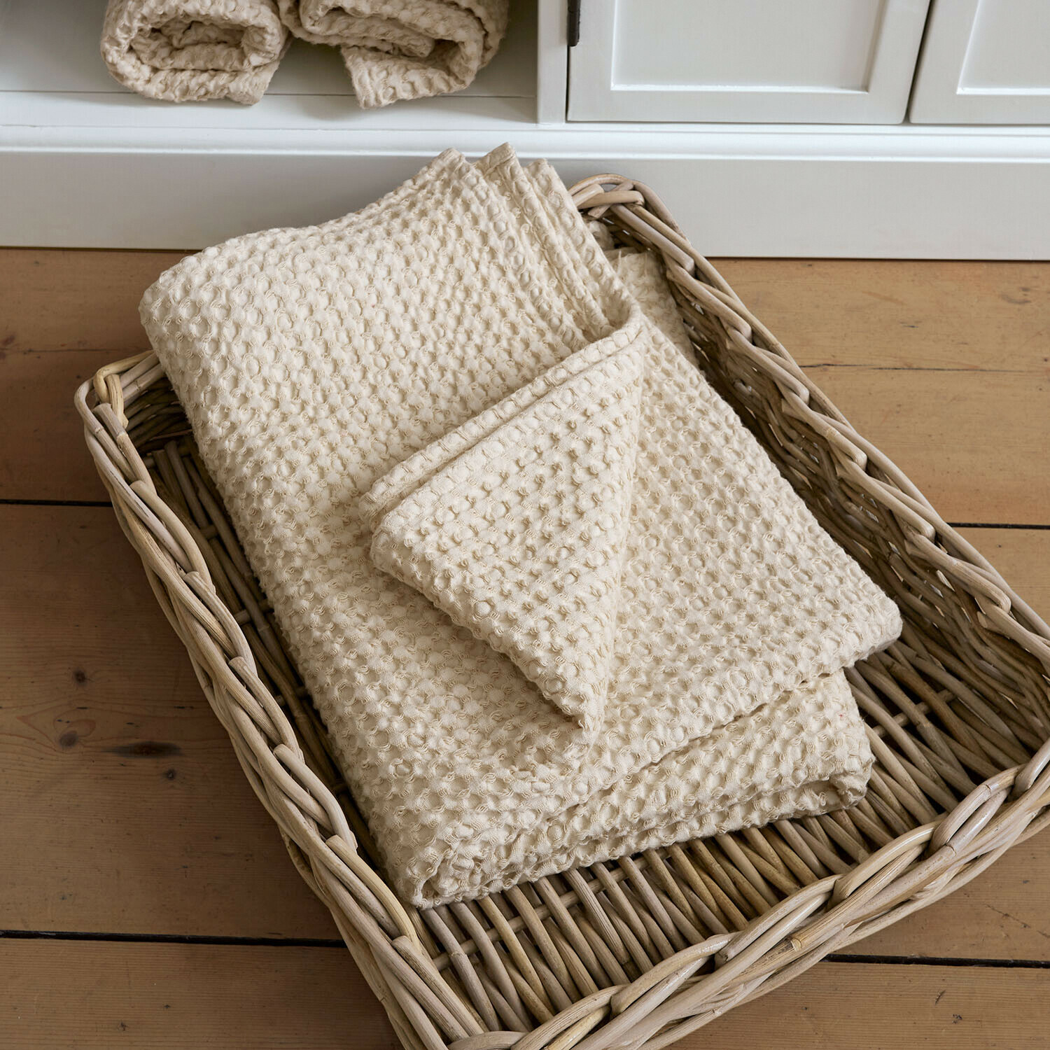Badetuch Maralei Cremefarbige Baumwolldecke mit Waffelstruktur in einem Rattankorb auf Holzboden