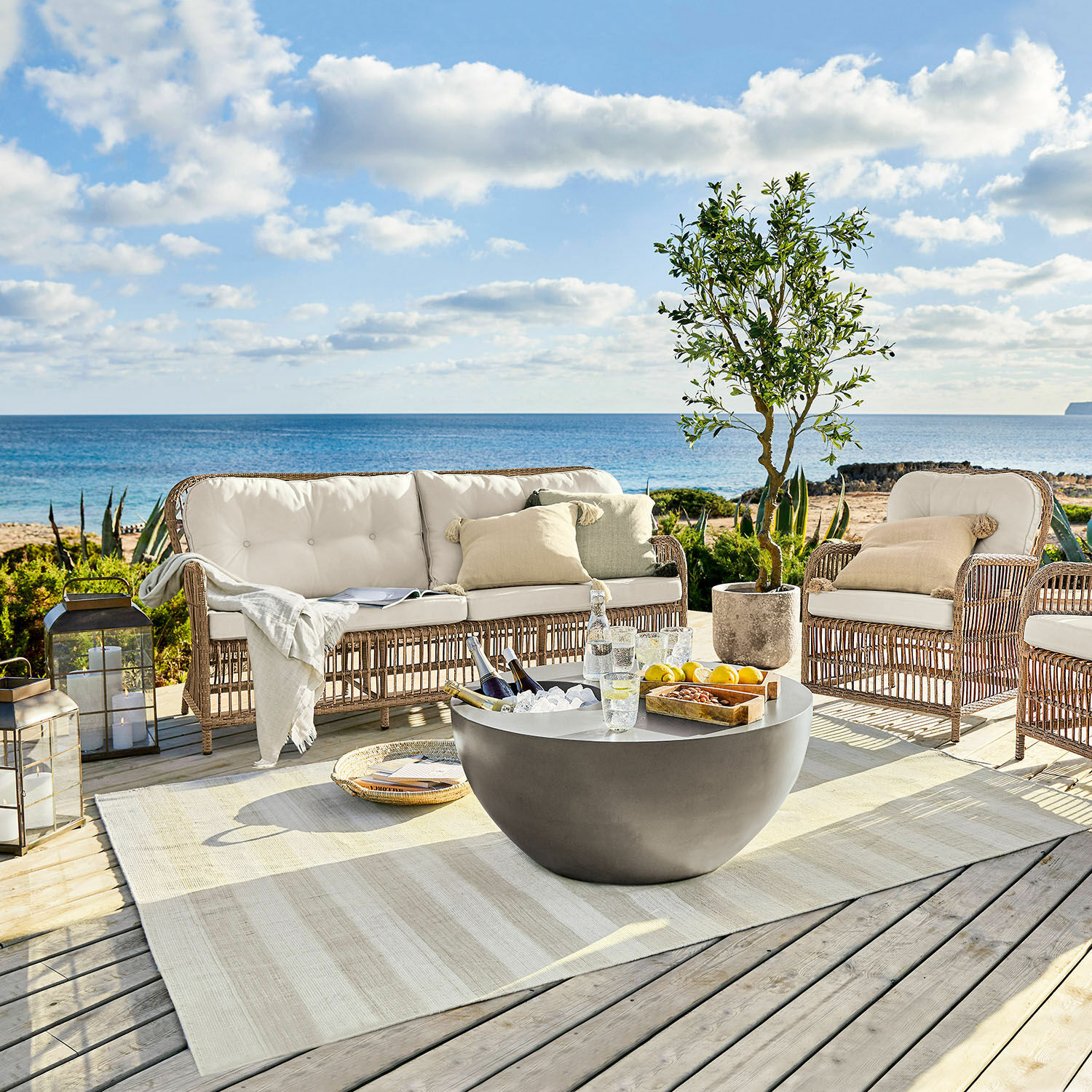 Gartenmöbel-Set aus Rattan mit cremefarbenen Polstern und Beton-Couchtisch auf Terrasse mit Meerblick