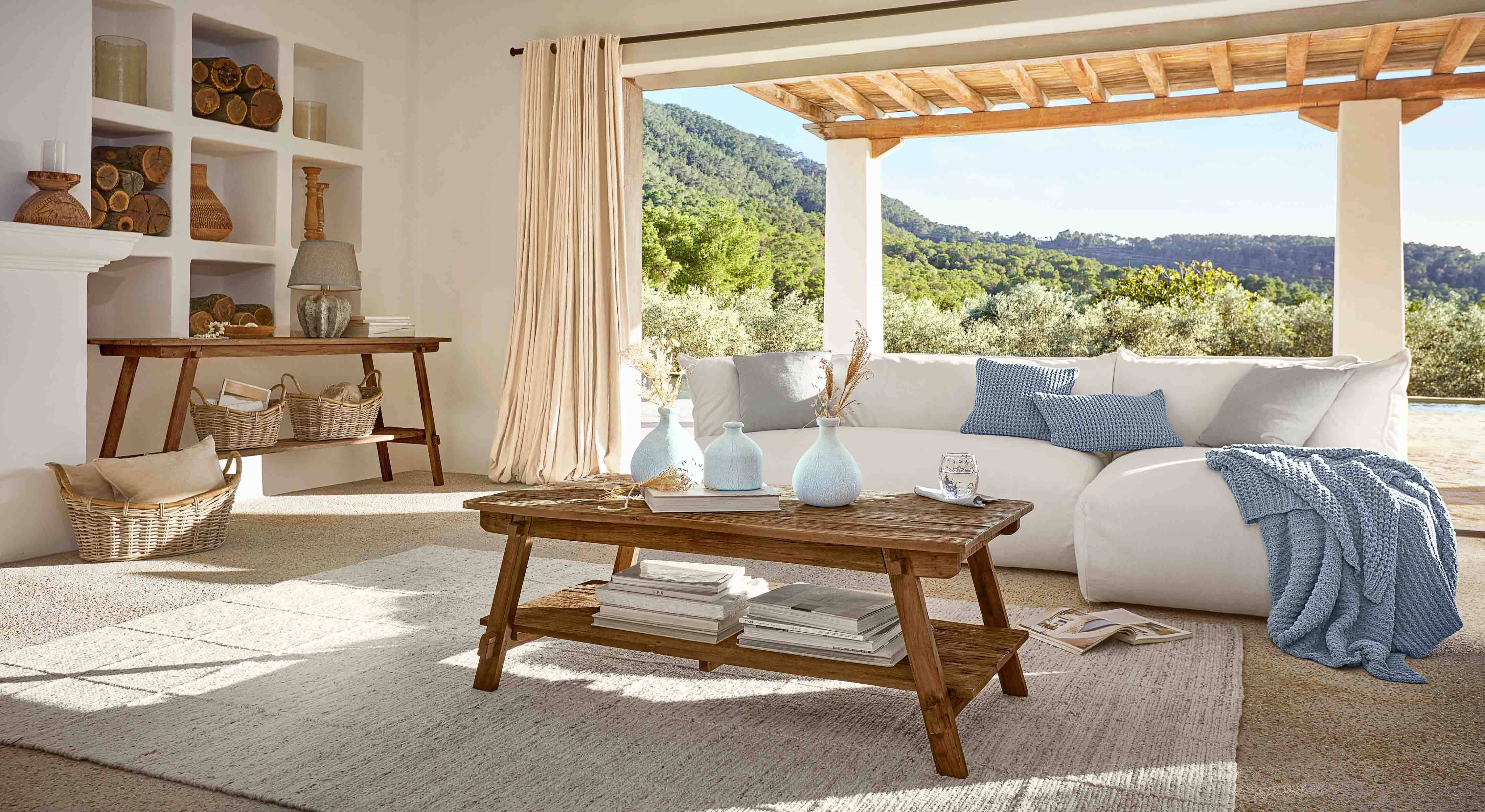 Helles Wohnzimmer mit rustikalem Holztisch und weißem Sofa mit blauer Decke und Kissen