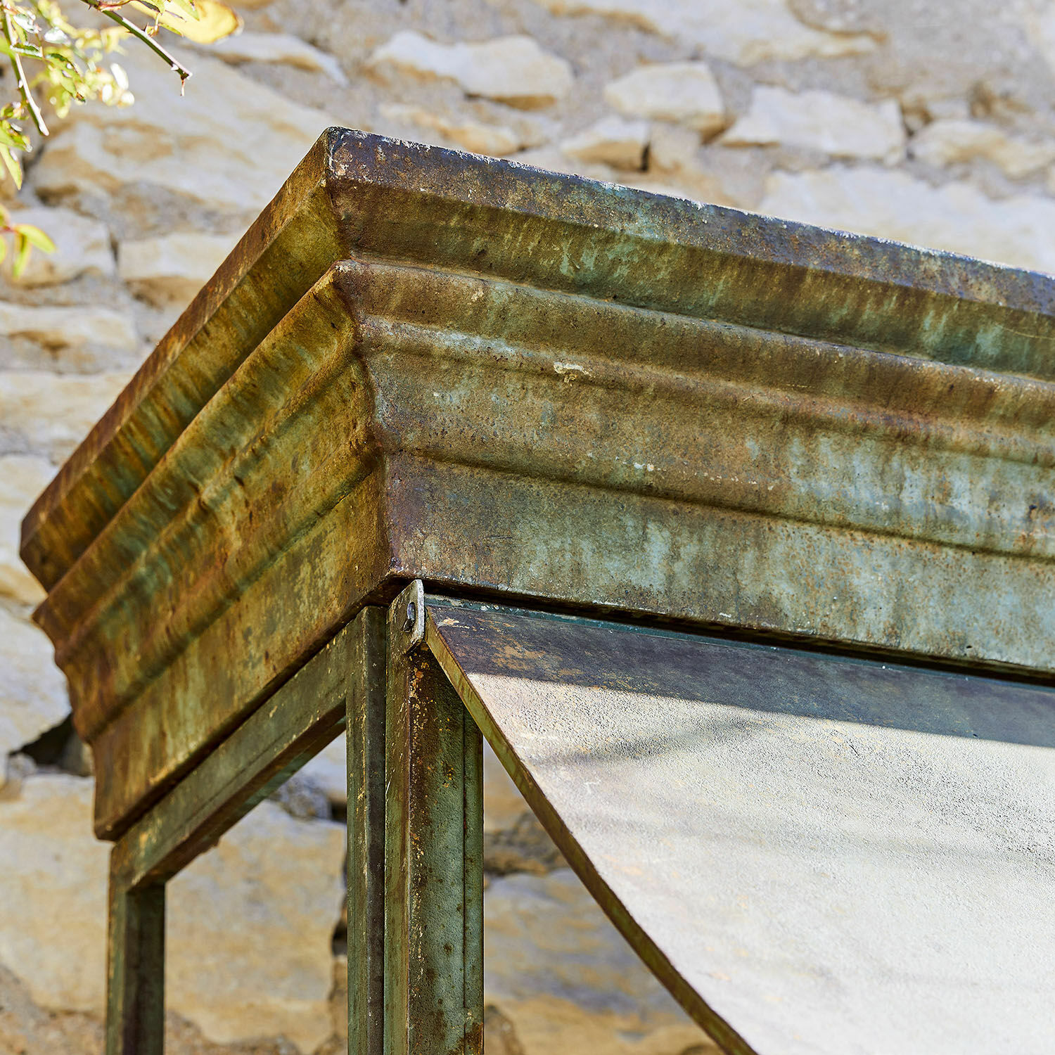 Grünlich patinierte Stahlkonstruktion mit geneigtem Dach vor Steinmauer, rustikale Gartendekoration