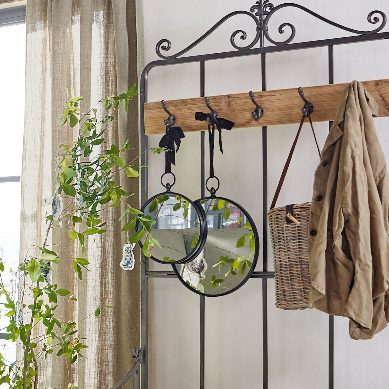 Metallgarderobe mit Holzleiste, runde Spiegel an schwarzen Bändern, beige Jacke und Korb aus Weide