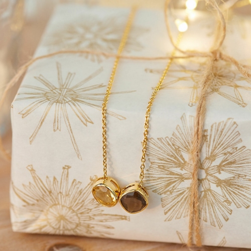 Goldene Halskette mit zwei Steinen auf Geschenkpapier mit goldenen Sternmotiven