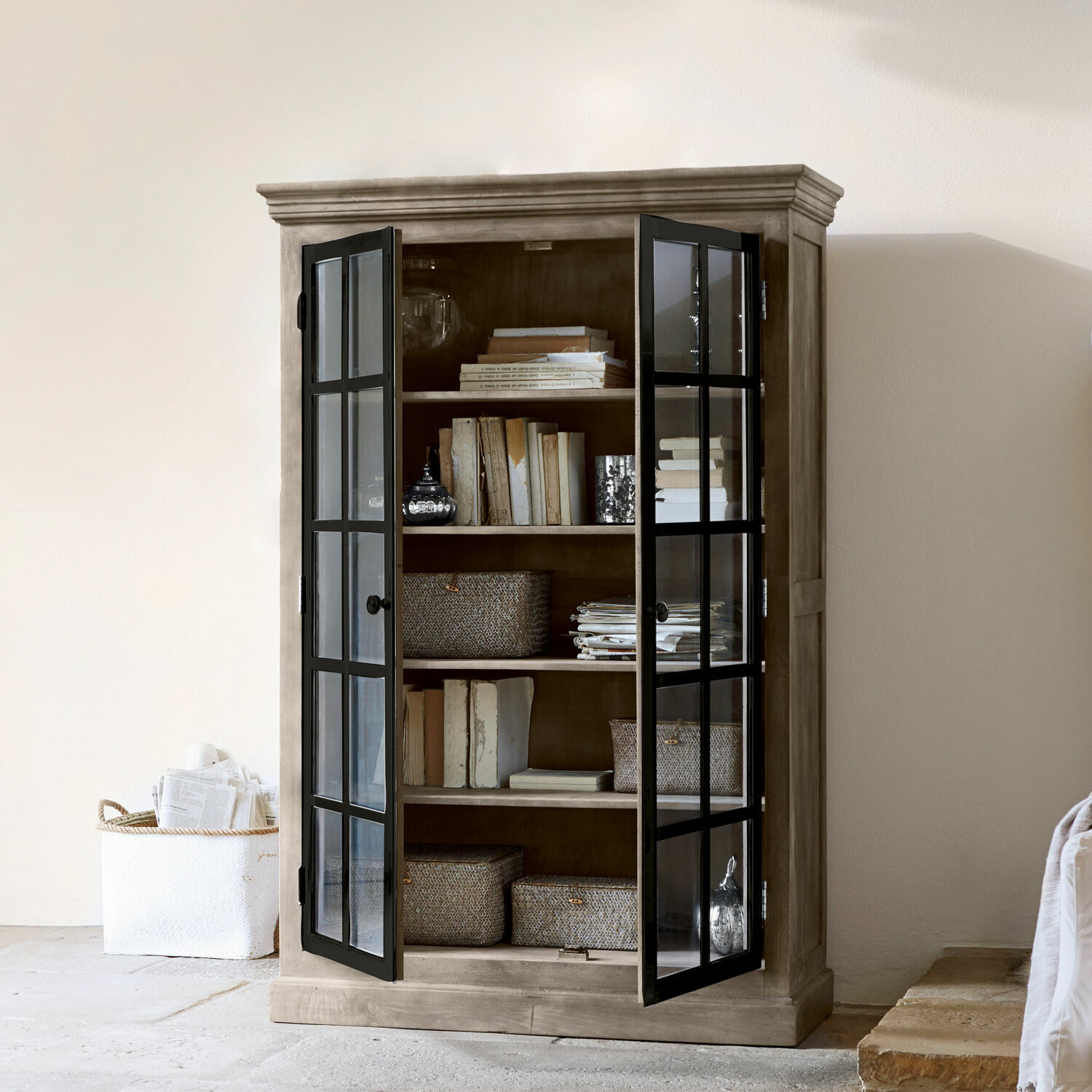 Holzschrank mit schwarzen Glastüren, gefüllt mit Büchern und Aufbewahrungskörben