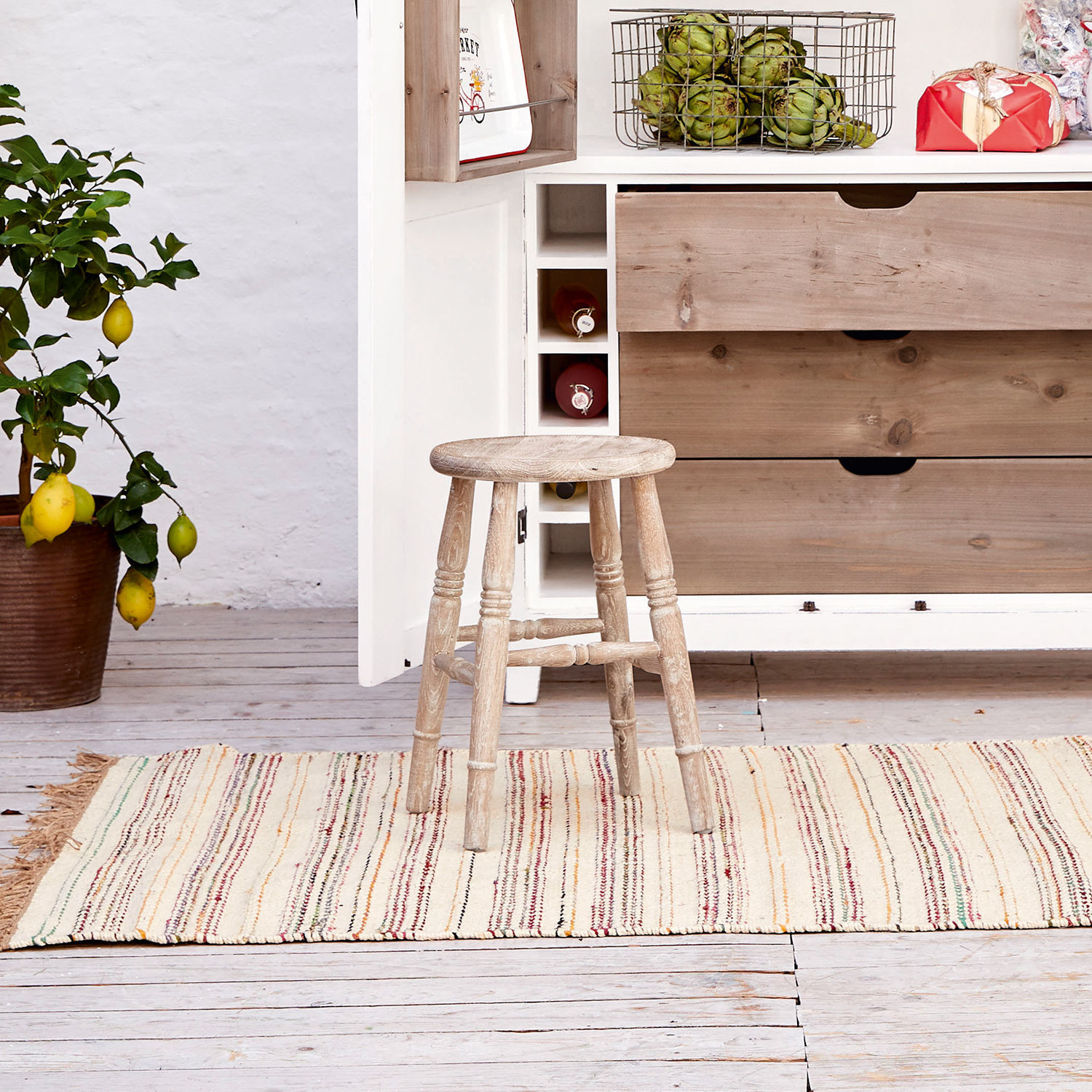 Holzhocker im Vintage-Stil auf buntem Teppich in hellem Küchenraum mit Zitronenbaum