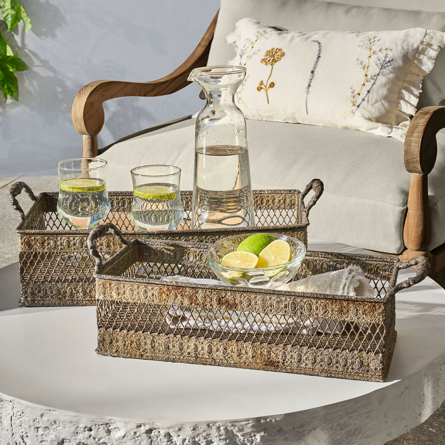 Zwei rustikale Metalltabletts mit Griffen auf weißem Tisch mit Karaffe und Gläsern mit Limettenwasser