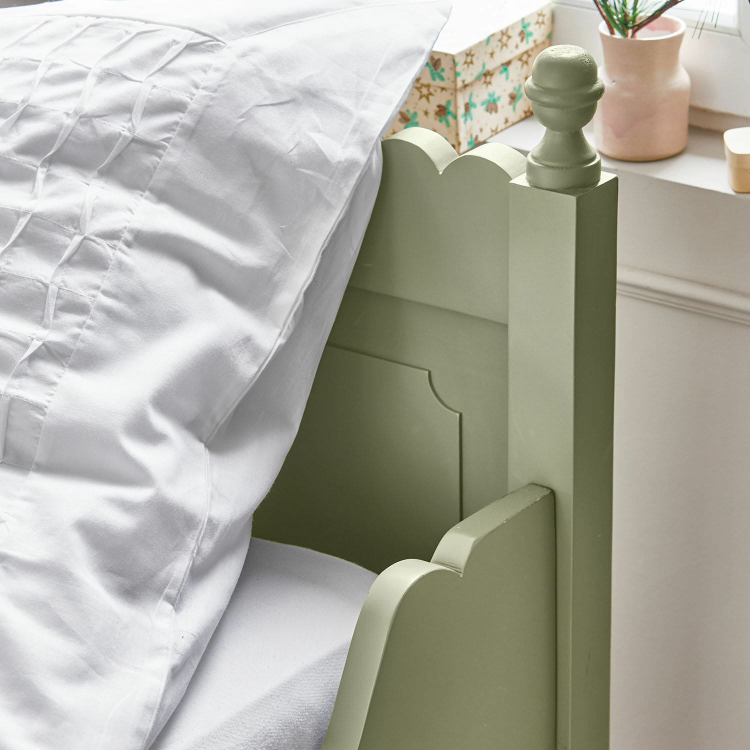 Grüner Holz-Bettrahmen mit dekorativem Pfosten und weißer Bettwäsche in hellem Zimmer