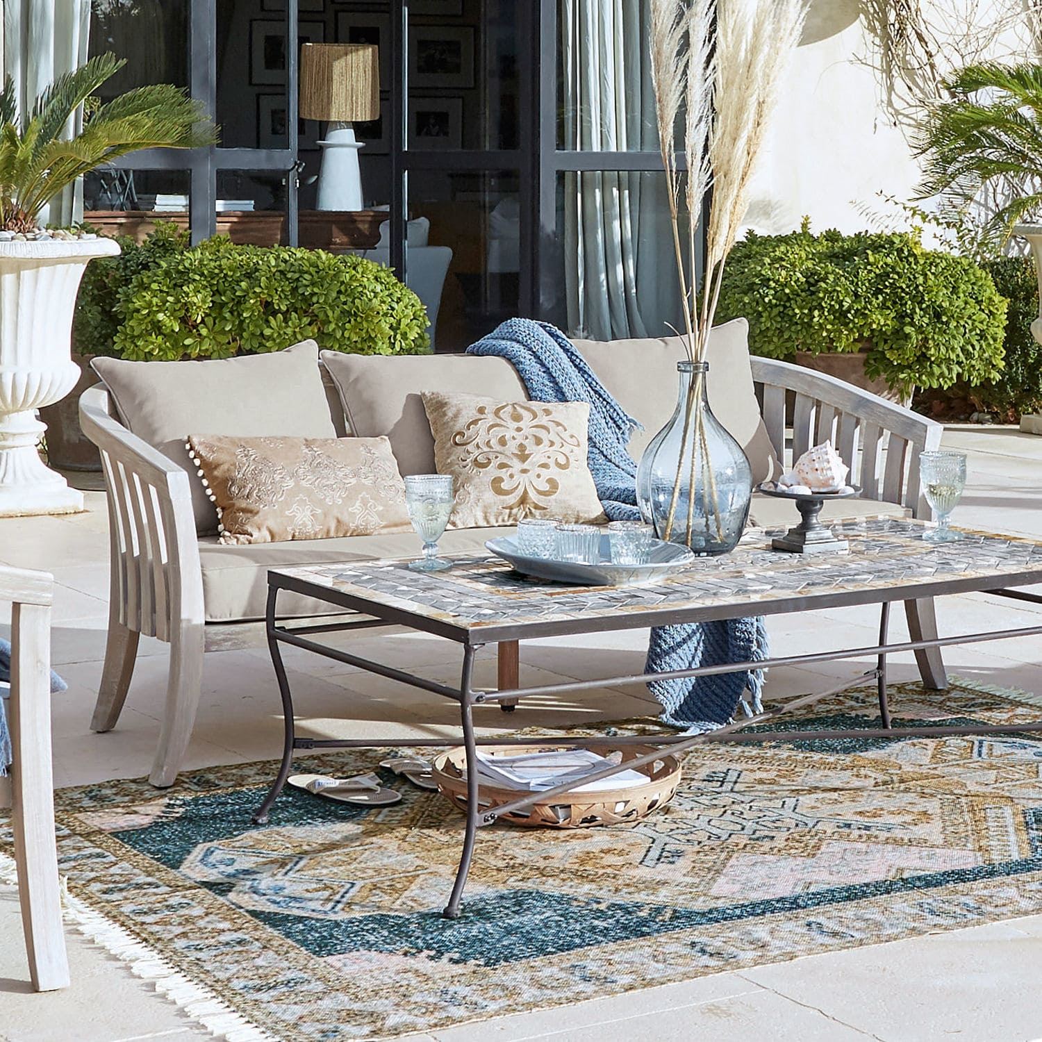 Beige Holz-Gartensofa mit Kissen und Metall-Couchtisch mit Mosaikplatte auf Terrasse