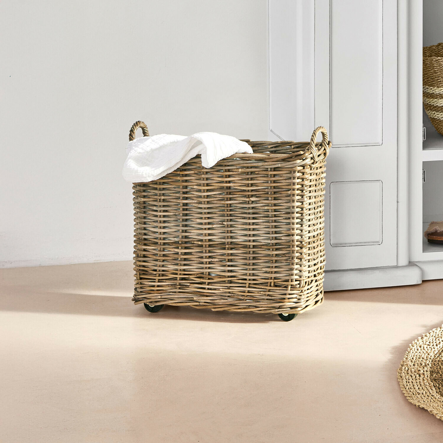 Wäschekorb aus natürlichem Weidengeflecht auf Rollen mit weißem Handtuch in hellem Raum