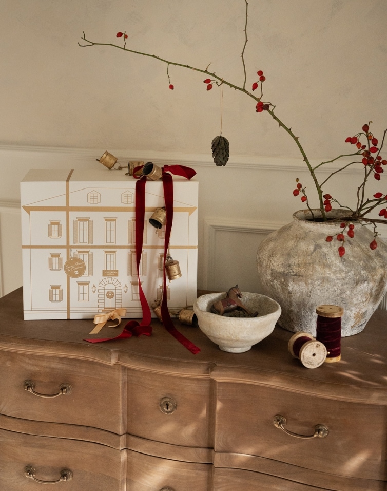 Weihnachtliche Dekoration mit weißer Geschenkbox, roten Bändern und natürlicher Keramik auf Holzkommode