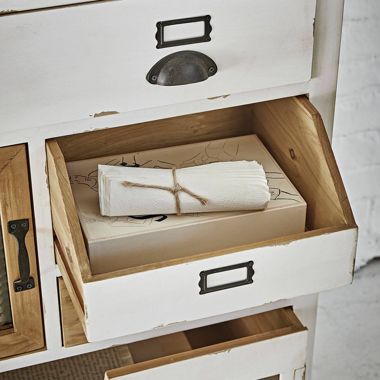 Weiße Holzschublade mit Metallgriff und naturfarbenem Innenraum mit Papierservietten.