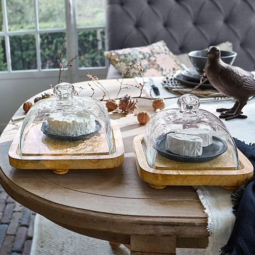 Holzbrett mit transparenter Glashaube für Käse auf dekorativ gedecktem Esstisch