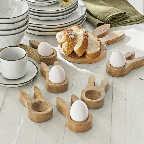 Holz-Eierhalter in Hasenohren-Form auf weißem Tisch mit Brot und Geschirr