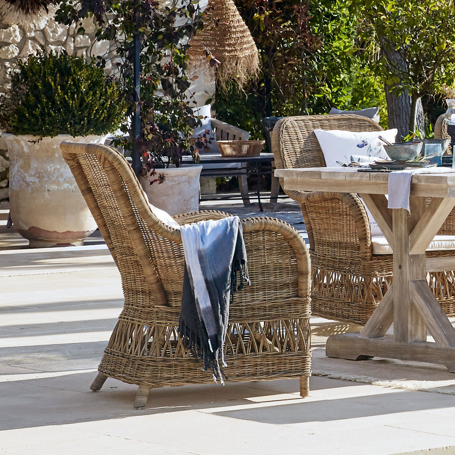 Rattansessel in Naturfarbe auf Terrasse mit Holztisch und dekorativen Kissen