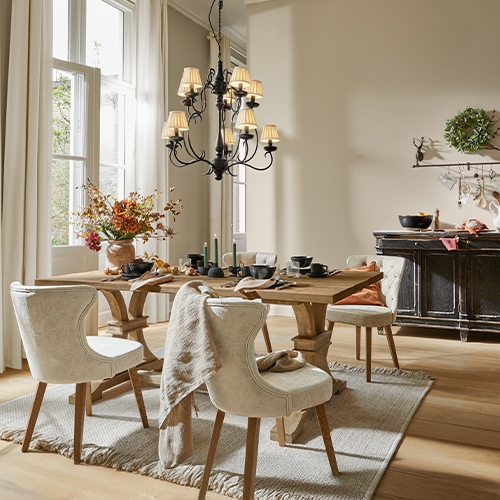 Esszimmer mit Holz-Tisch, cremefarbenen Polsterstühlen, Blumenarrangement und schwarzem Kronleuchter