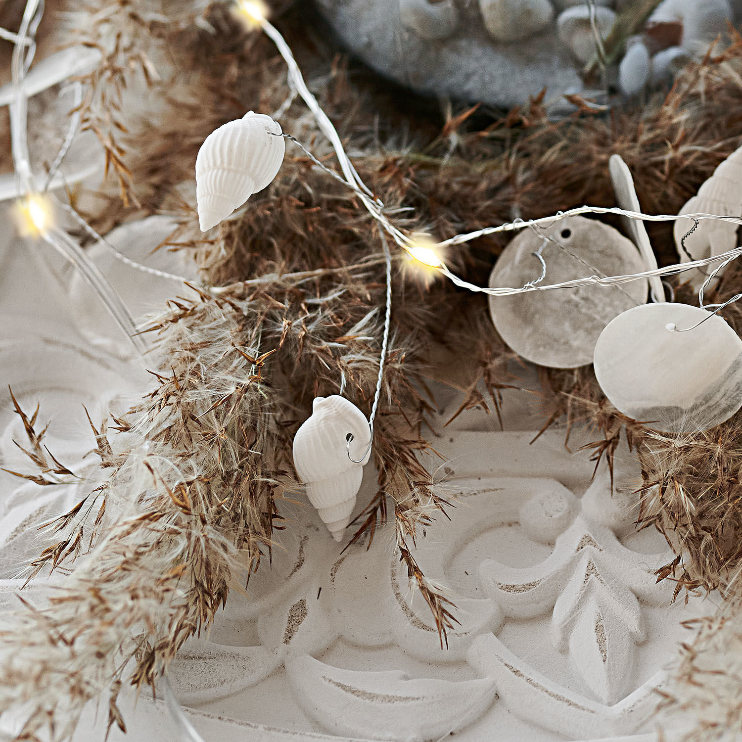 Dekorative Lichterkette mit weißen Muscheln und Naturgras auf hellem Hintergrund