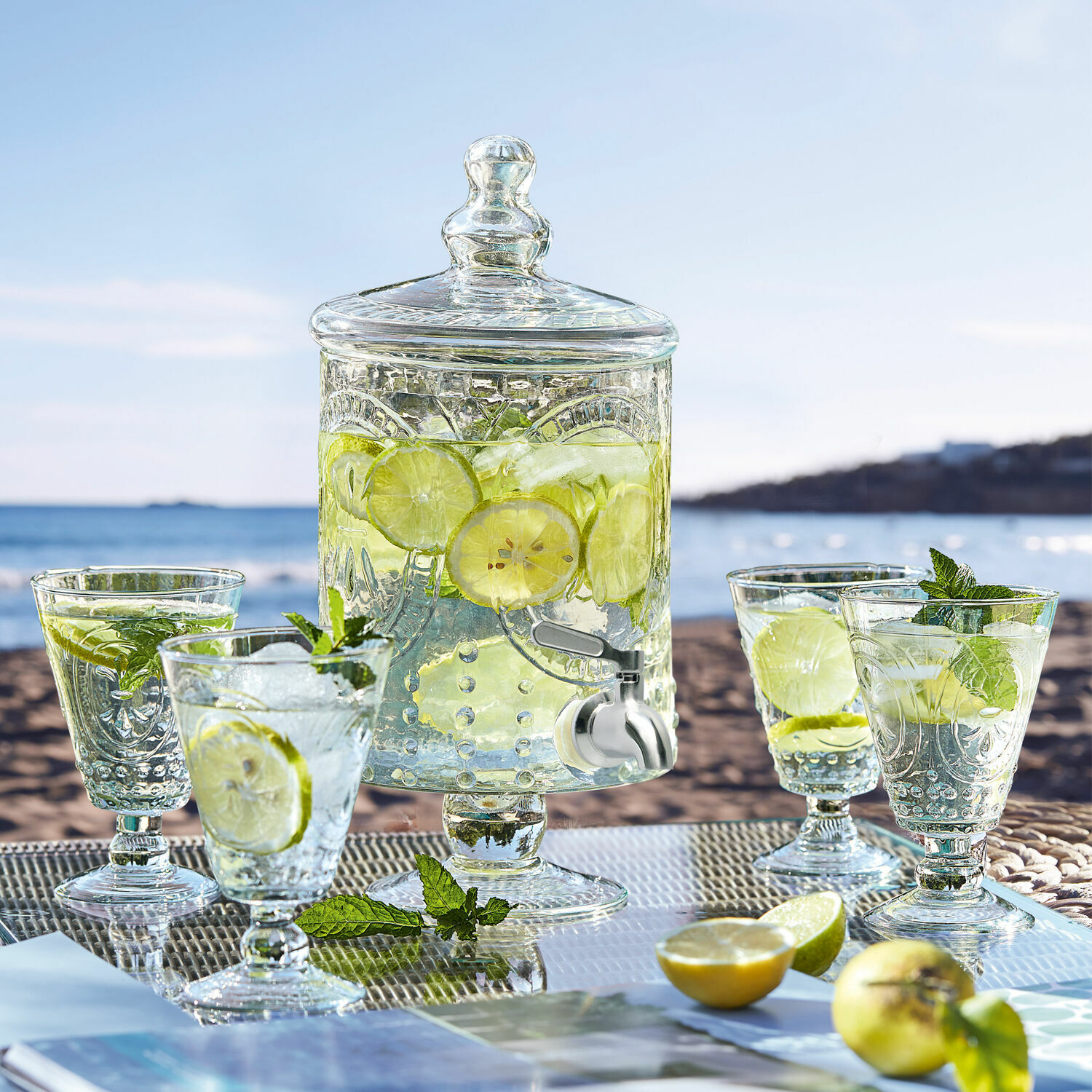 Glasgetränkespender mit Deckel und Zapfhahn, gefüllt mit Zitronen-Minz-Wasser am Strand