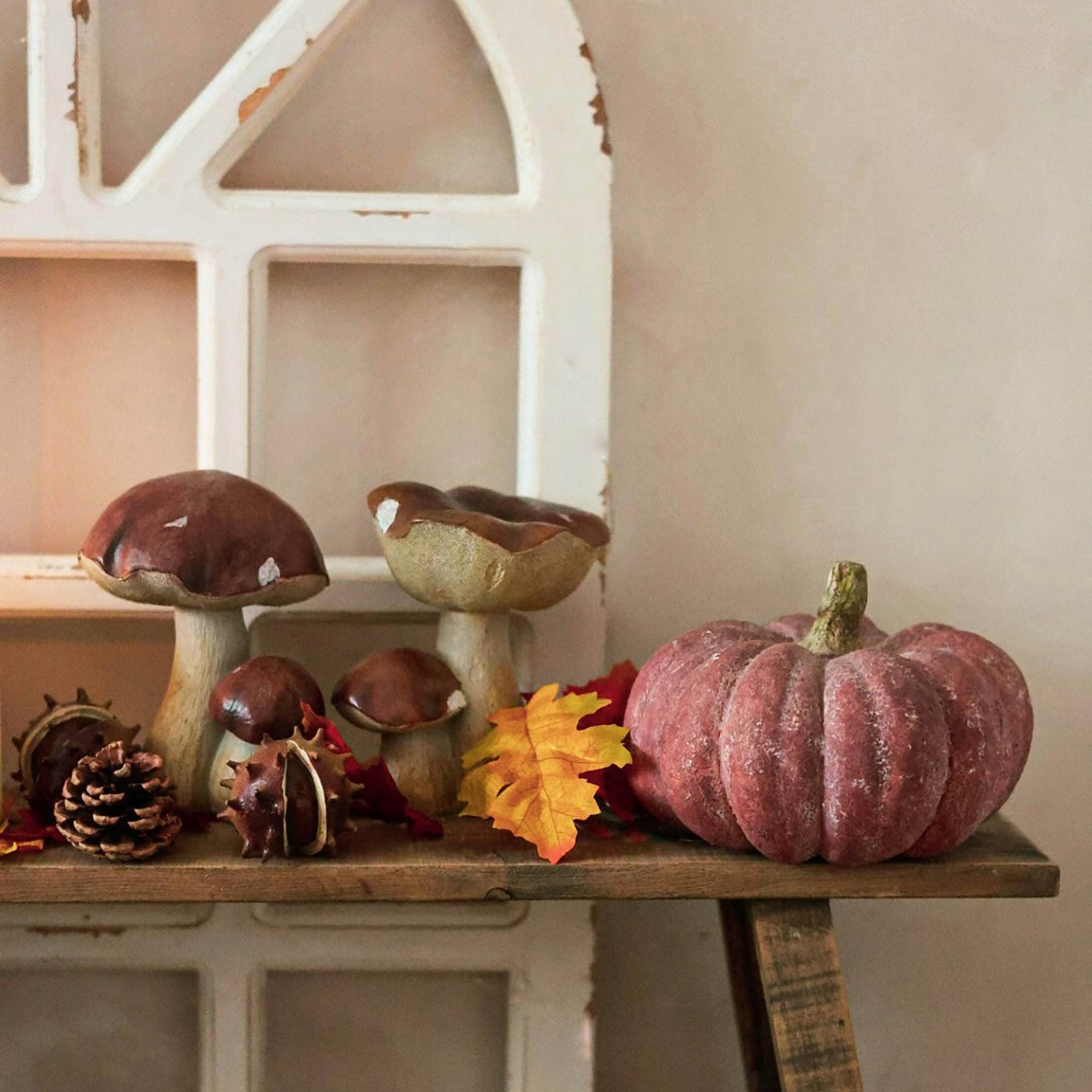 Herbstliche Dekoration mit Keramikpilzen und rosa Kürbis auf rustikalem Holzregal