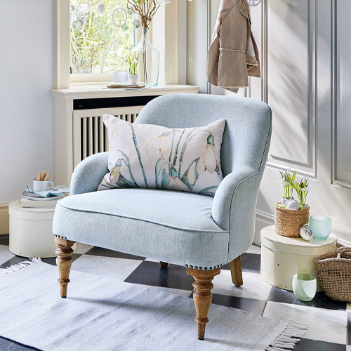 Hellblauer Polsterstuhl mit Holzbeinen und dekorativem Kissen in hellem Raum