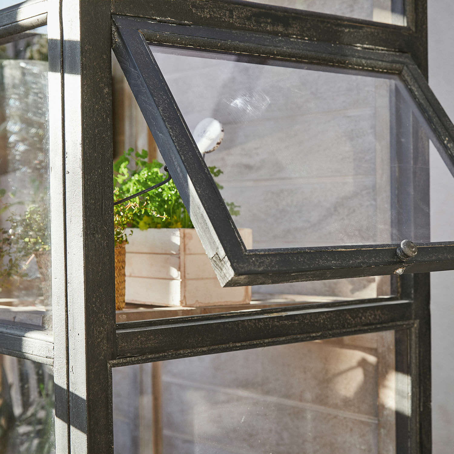 Schwarzer Metall-Gartenschrank mit aufklappbarem Fenster und Pflanze in Holzkiste innen