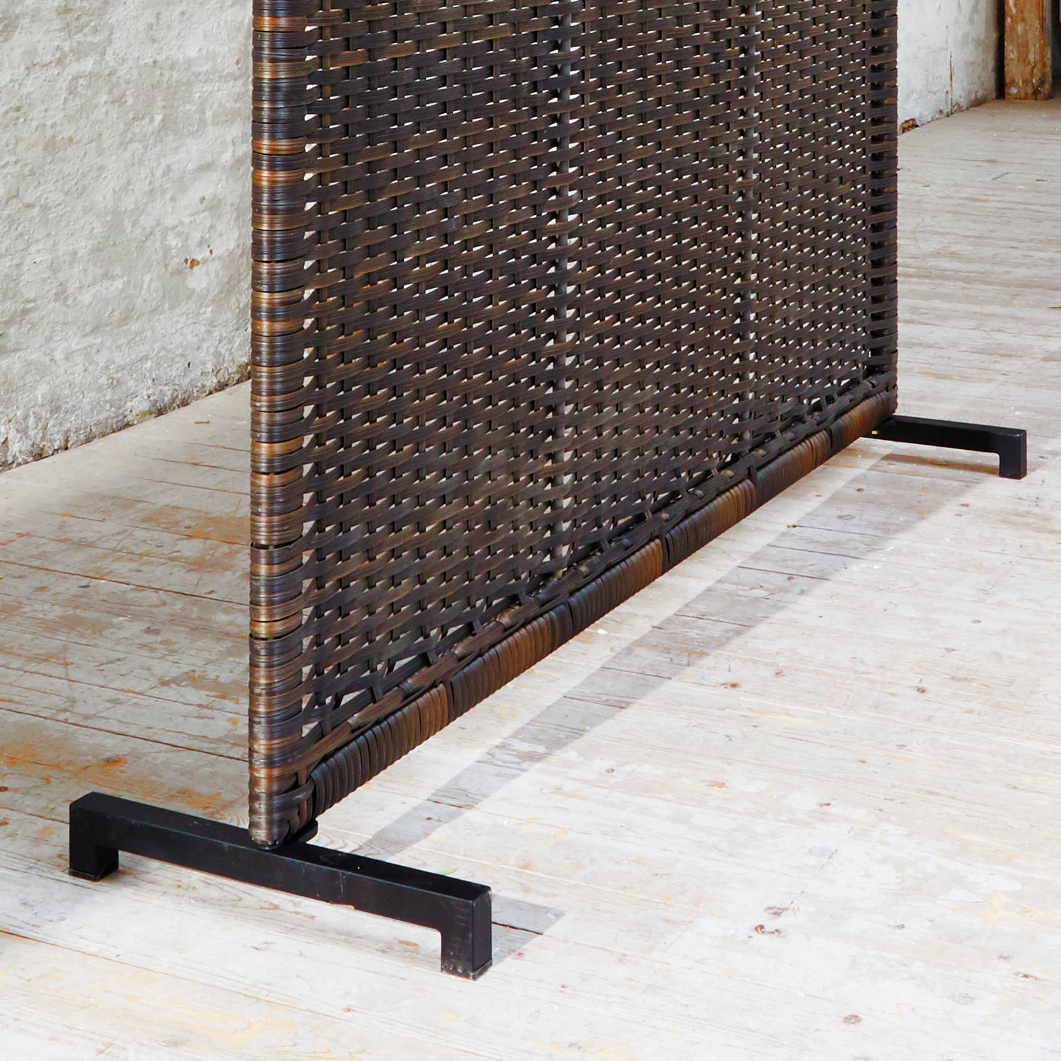 Raumteiler aus dunklem Rattan mit Metallfuß auf hellem Holzboden, modernes Wohnaccessoire