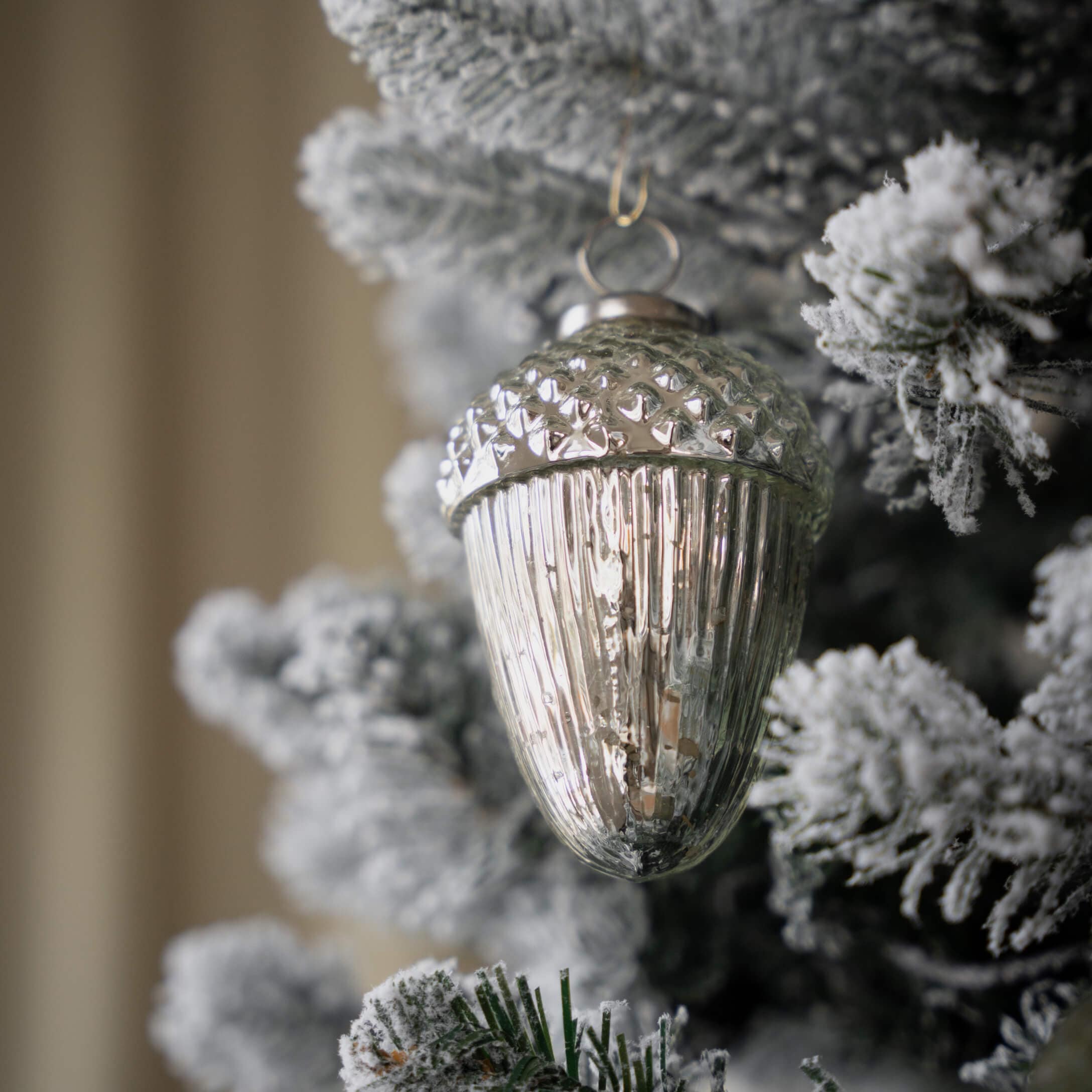 Silberne Glas-Weihnachtsbaumkugel in Form einer Eichel an schneebedecktem Tannenbaum