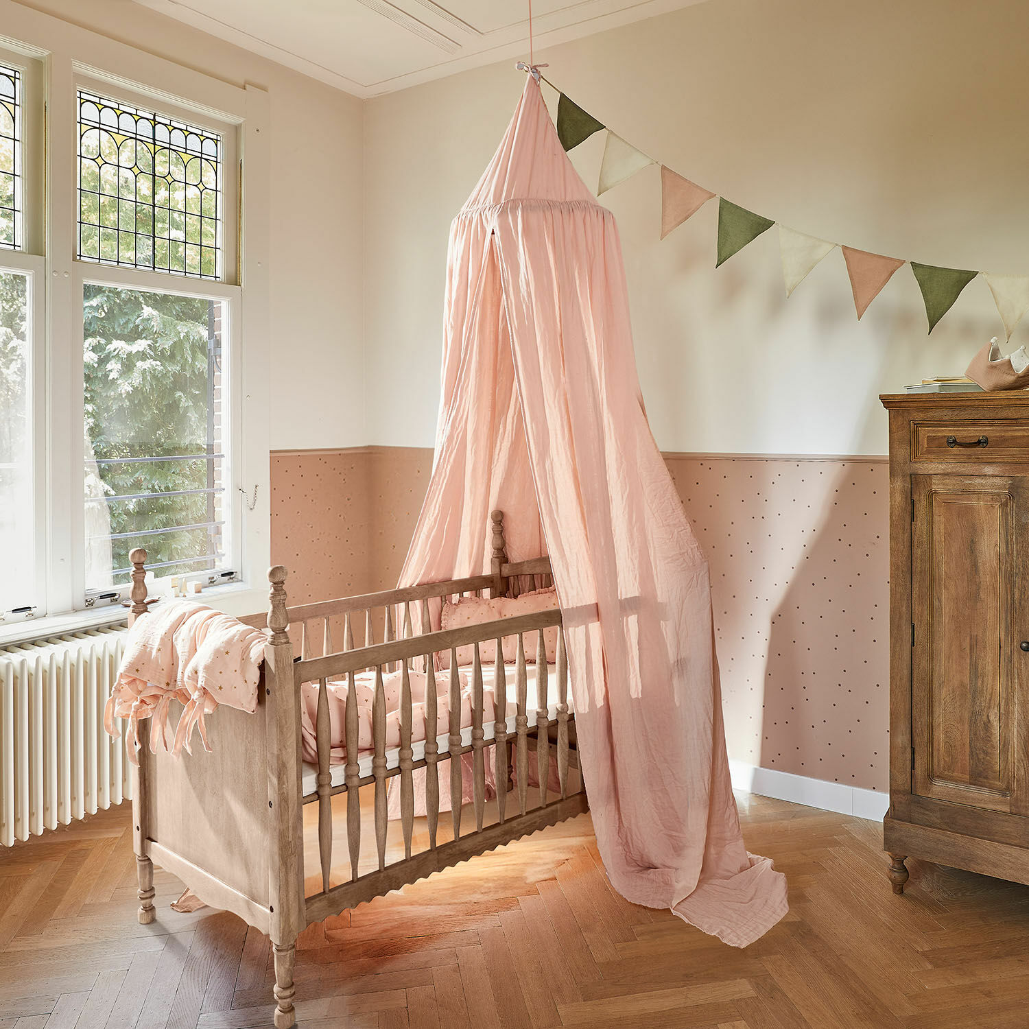 Babybett Merveillon Kinderbett aus Holz mit rosa Baldachin und passender Bettwäsche in pastellfarbenem Kinderzimmer