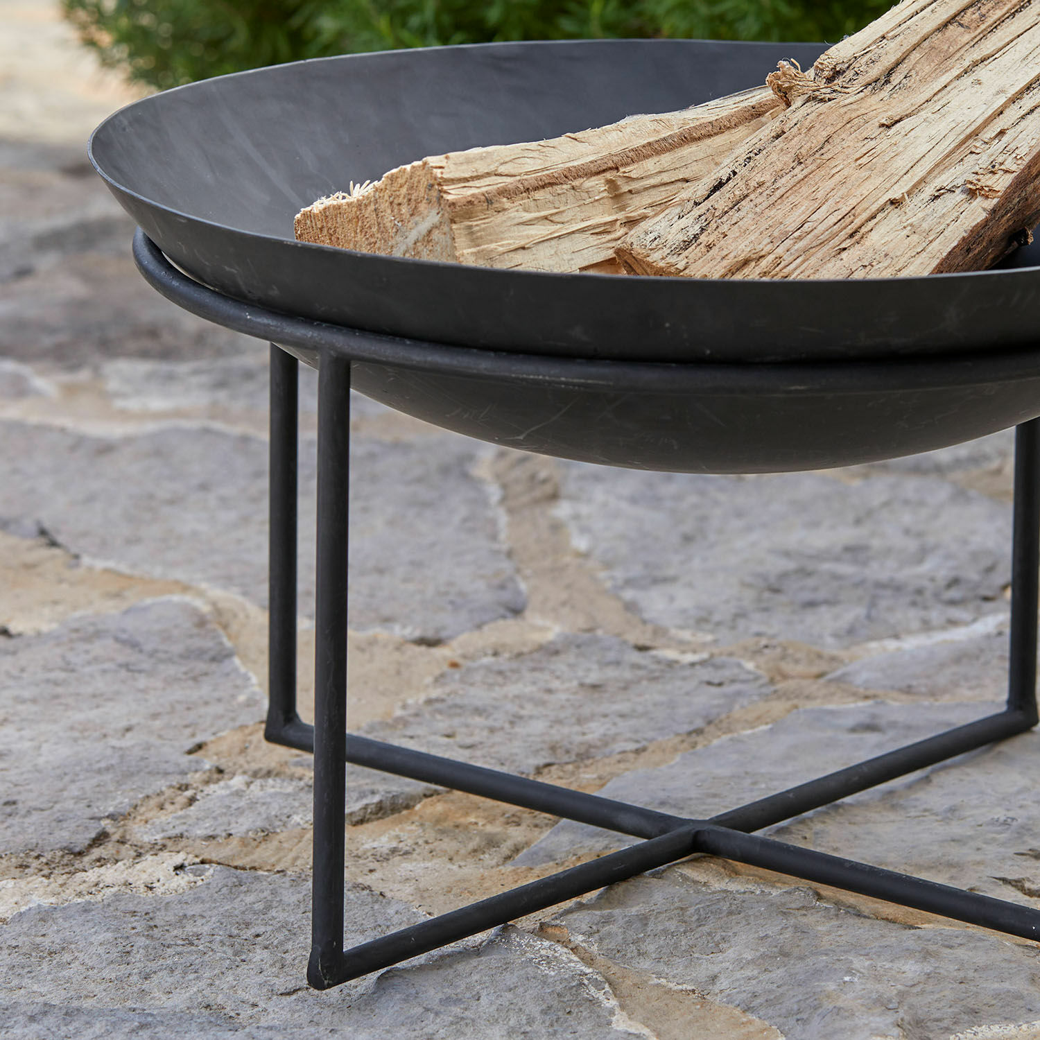 Schwarzes Metall-Feuerkorb mit Holzscheiten auf Steinboden für den Garten