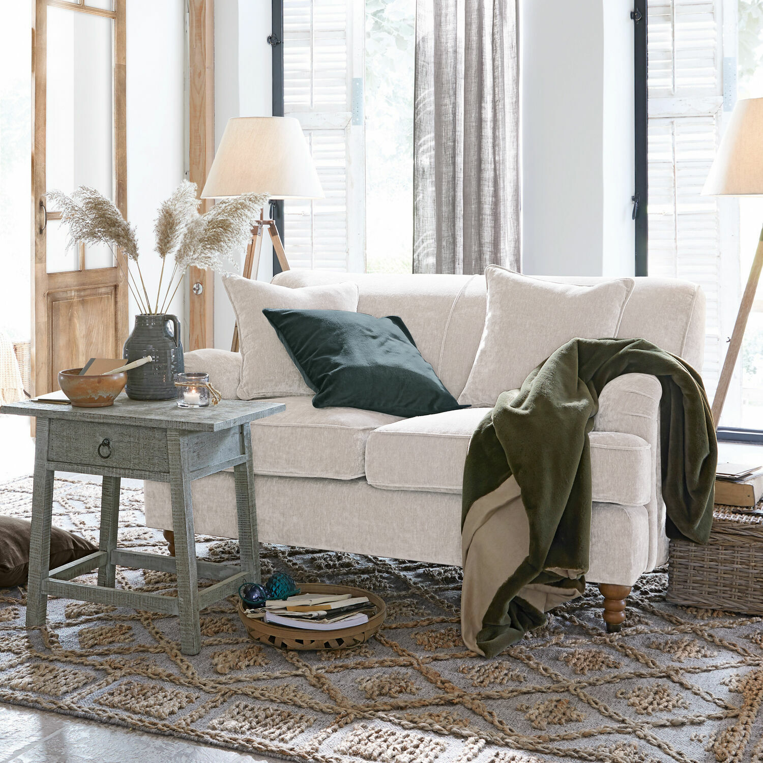 Beiges Sofa aus weichem Stoff mit grünem Überwurf und Kissen in gemütlichem Wohnzimmer mit Holztisch