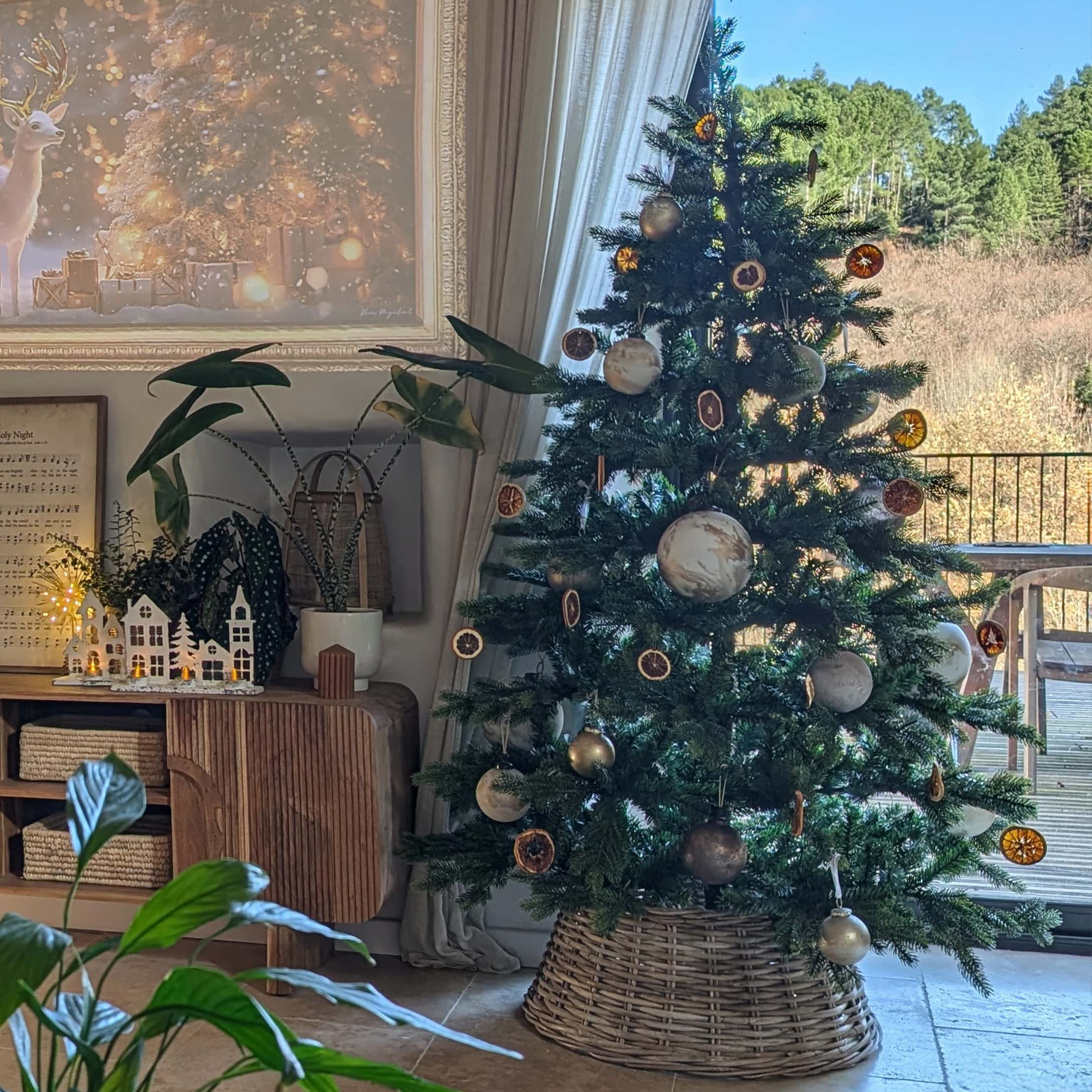 Weihnachtsbaum im Korb aus Weide mit natürlichen Anhängern und hellen Kugeln in gemütlichem Raum