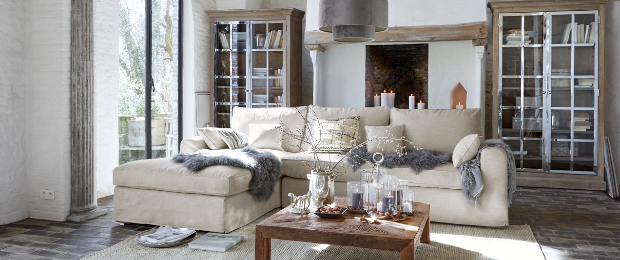 Beige Ecksofa aus weichem Stoff in hellem Wohnzimmer mit Holztisch und Kamin