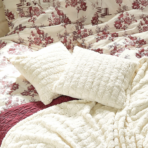 Weiche cremefarbene Plüschkissen und Decke auf Bett mit bordeauxfarbenem Blumenmuster