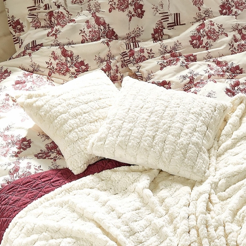 Weiche cremefarbene Plüschkissen und Decke auf Bett mit bordeauxfarbenem Blumenmuster