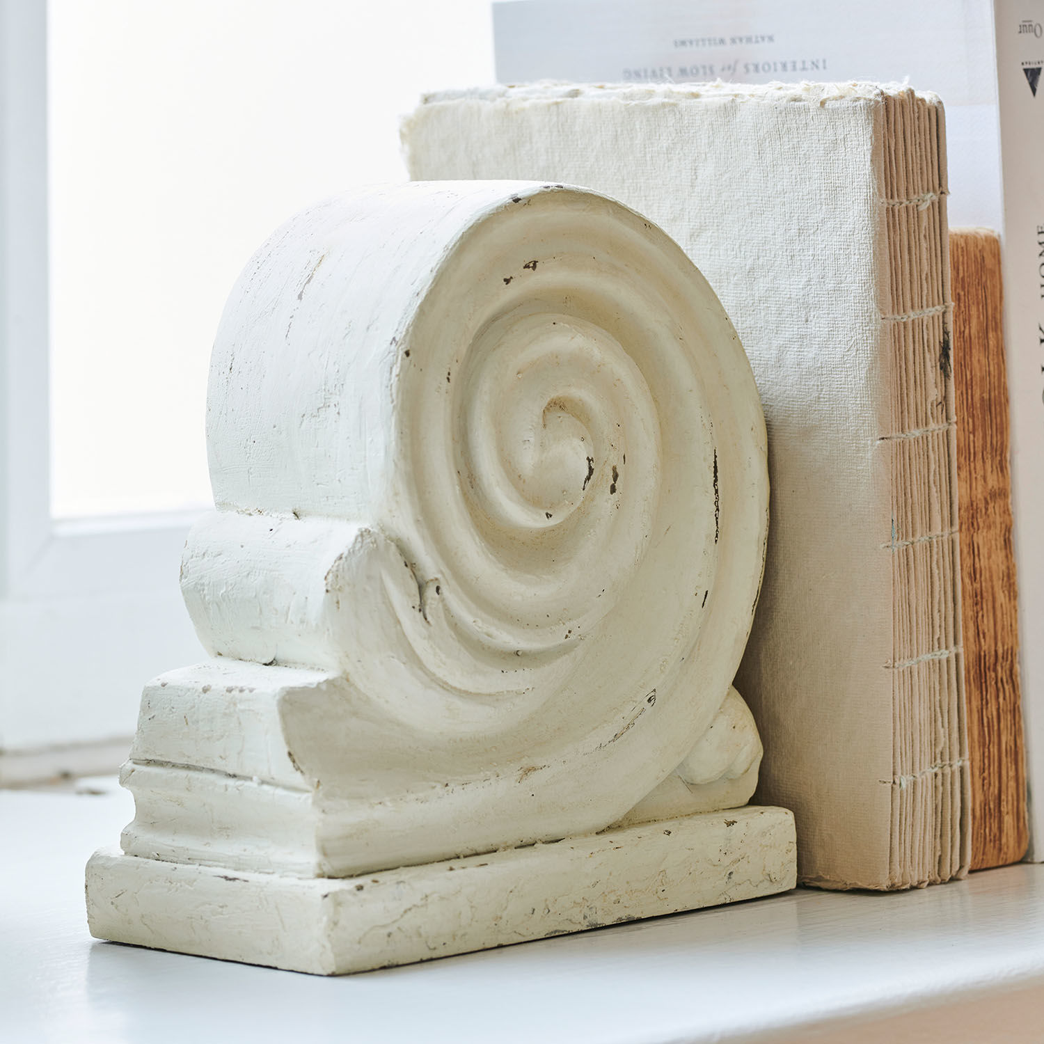 Weißes dekoratives Steinelement mit Spiralornament neben Büchern auf Fensterbank
