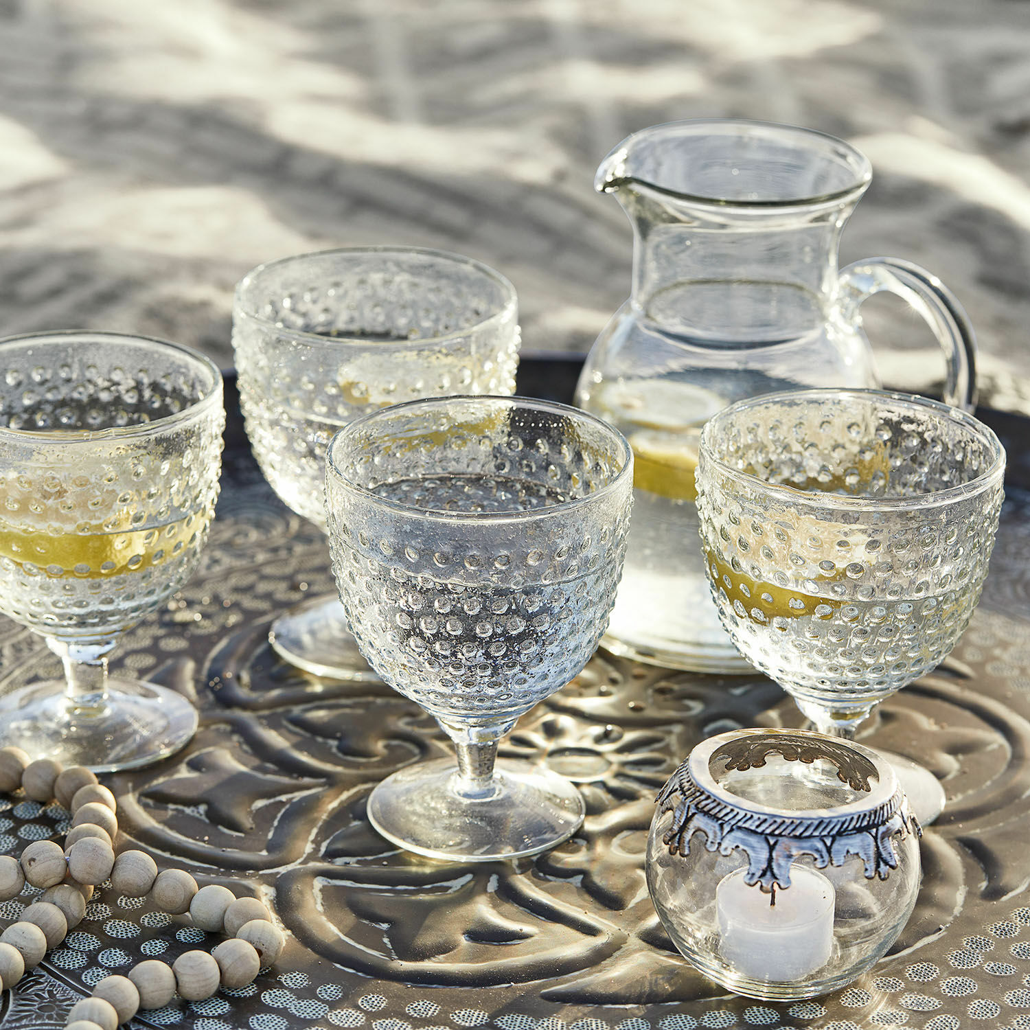 Gläser und Krug aus klarem Glas mit Noppenmuster auf Metalltablett mit Zitrone und Kerze