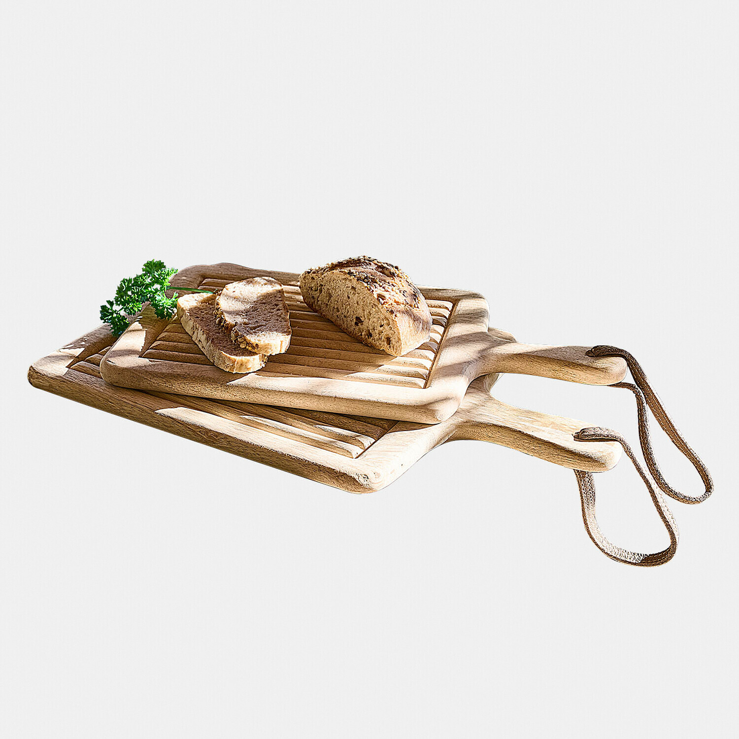 Holz-Schneidebretter mit Griffen und Lederbändern, darauf geschnittenes Brot und frische Petersilie, naturfarben