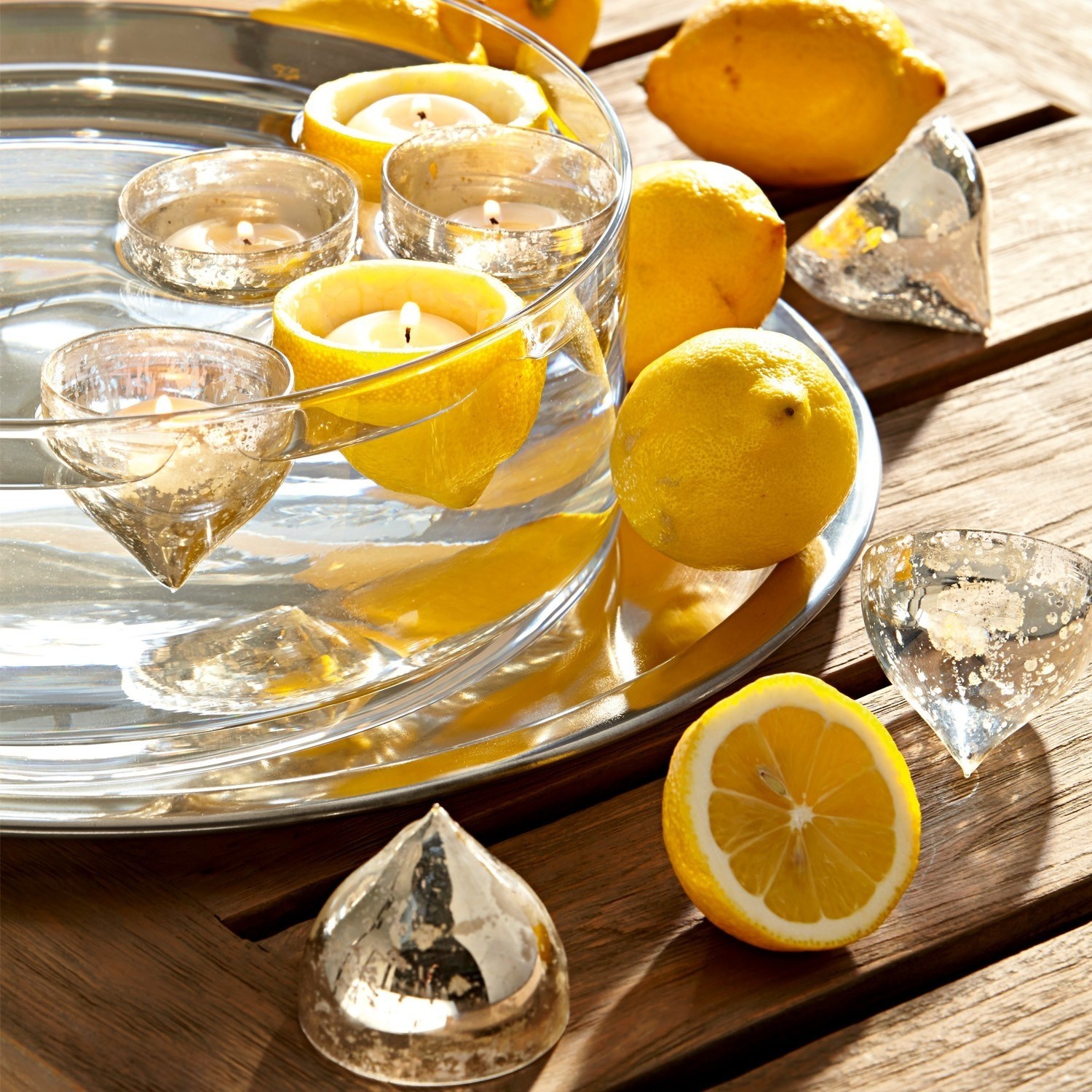 Glas-Schale mit schwimmenden Kerzen in Zitronen auf Holztisch mit Dekoration