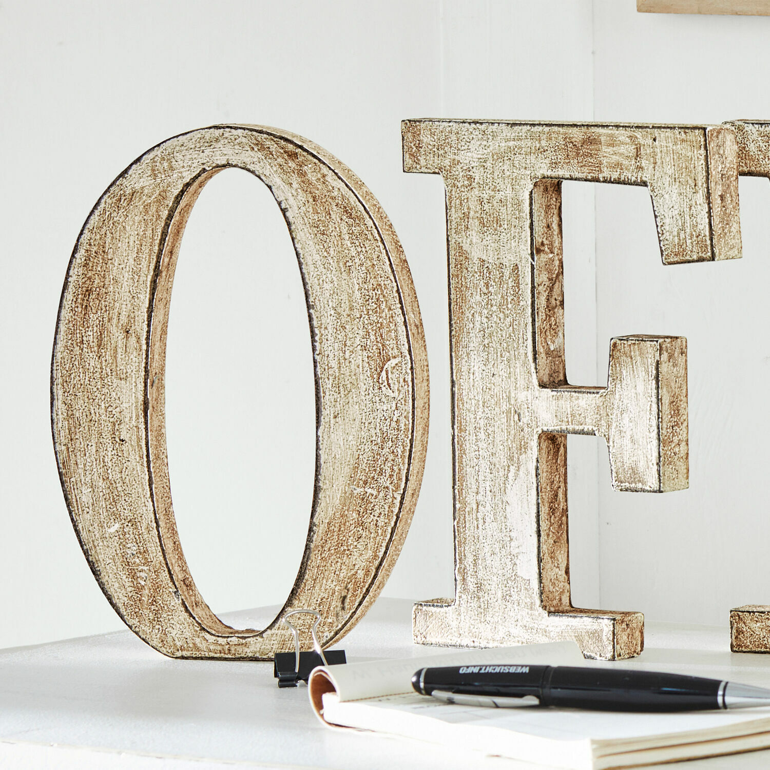 Dekorative Holzbuchstaben O und E in weißem Used-Look auf weißem Tisch mit Notizbuch und Stift