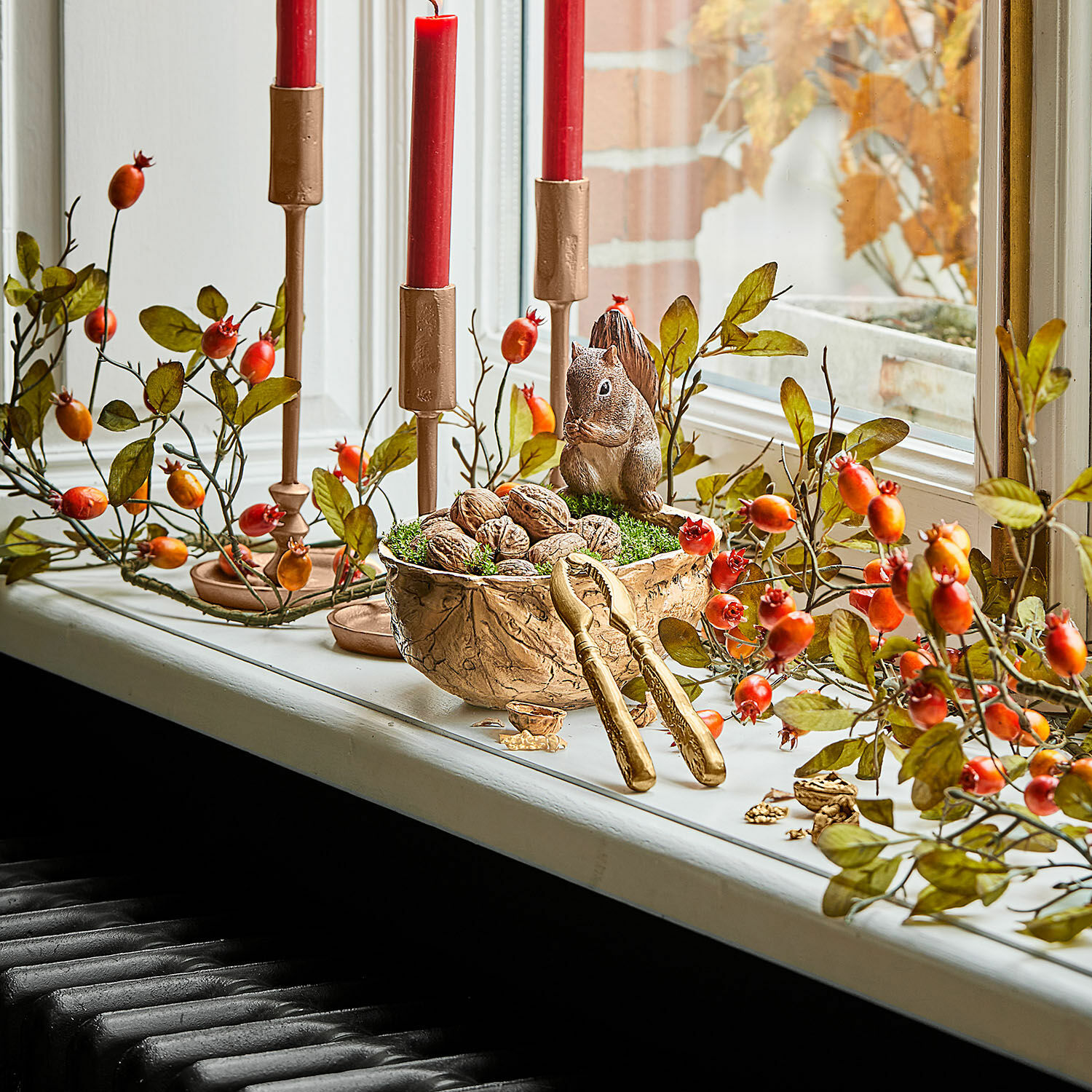 Herbstliche Fensterdekoration mit roten Kerzen, Walnüssen und Eichhörnchenfigur in Naturtönen