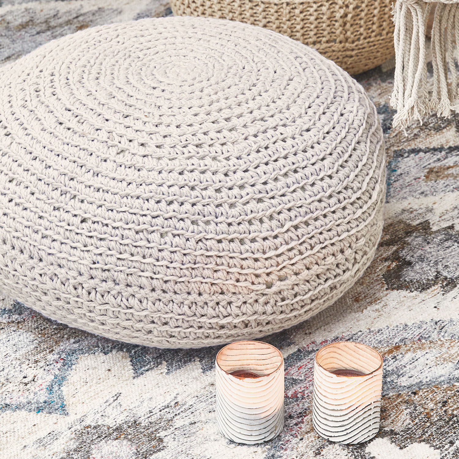 Runder beiger Pouf aus geflochtenem Material auf gemustertem Teppich mit zwei Kerzenhaltern