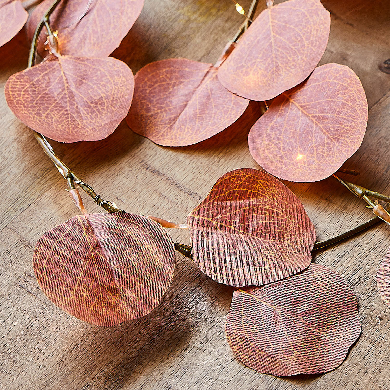 Dekorative Lichterkette mit rosa Stoffblättern auf Holzuntergrund, stimmungsvolle Beleuchtung