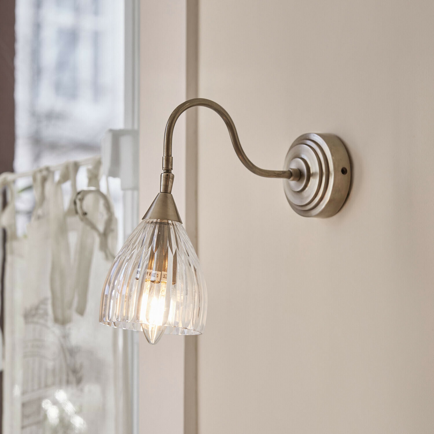 Wandlampe Niamhs Wandleuchte mit klarem Glaslampenschirm und gebogenem Metallarm in antik-silberner Farbe