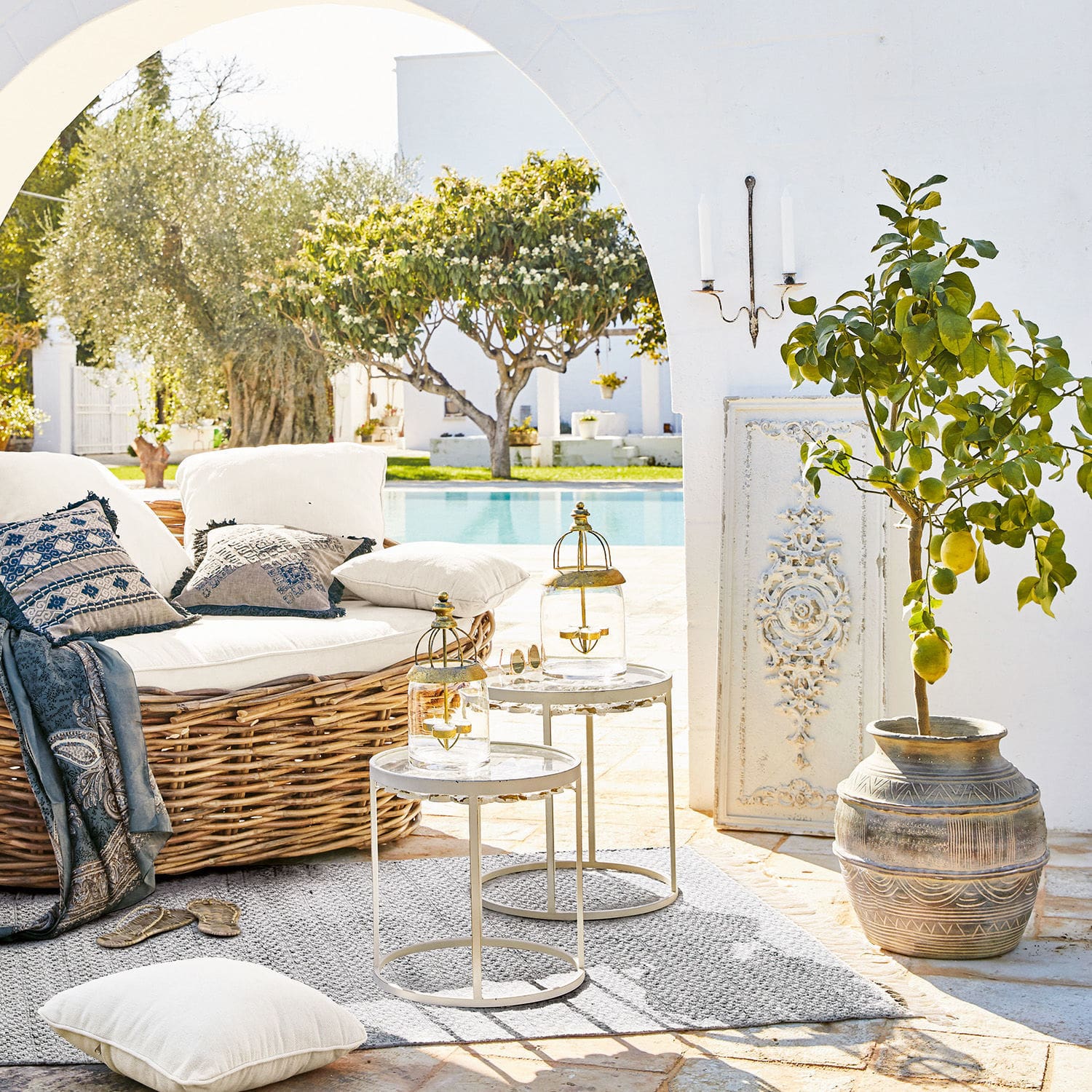 Gemütliche Rattan-Eckcouch mit weißen Kissen und zwei Metall-Beistelltischen auf Terrasse am Pool