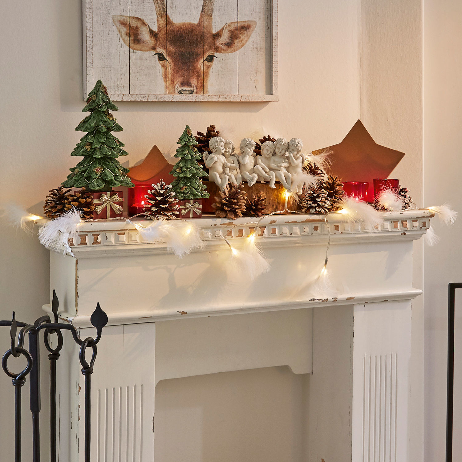 Weihnachtliche Kamin-Dekoration mit grünen Tannen, Engeln, Kiefernzapfen und roten Kerzen für gemütliche Stimmung