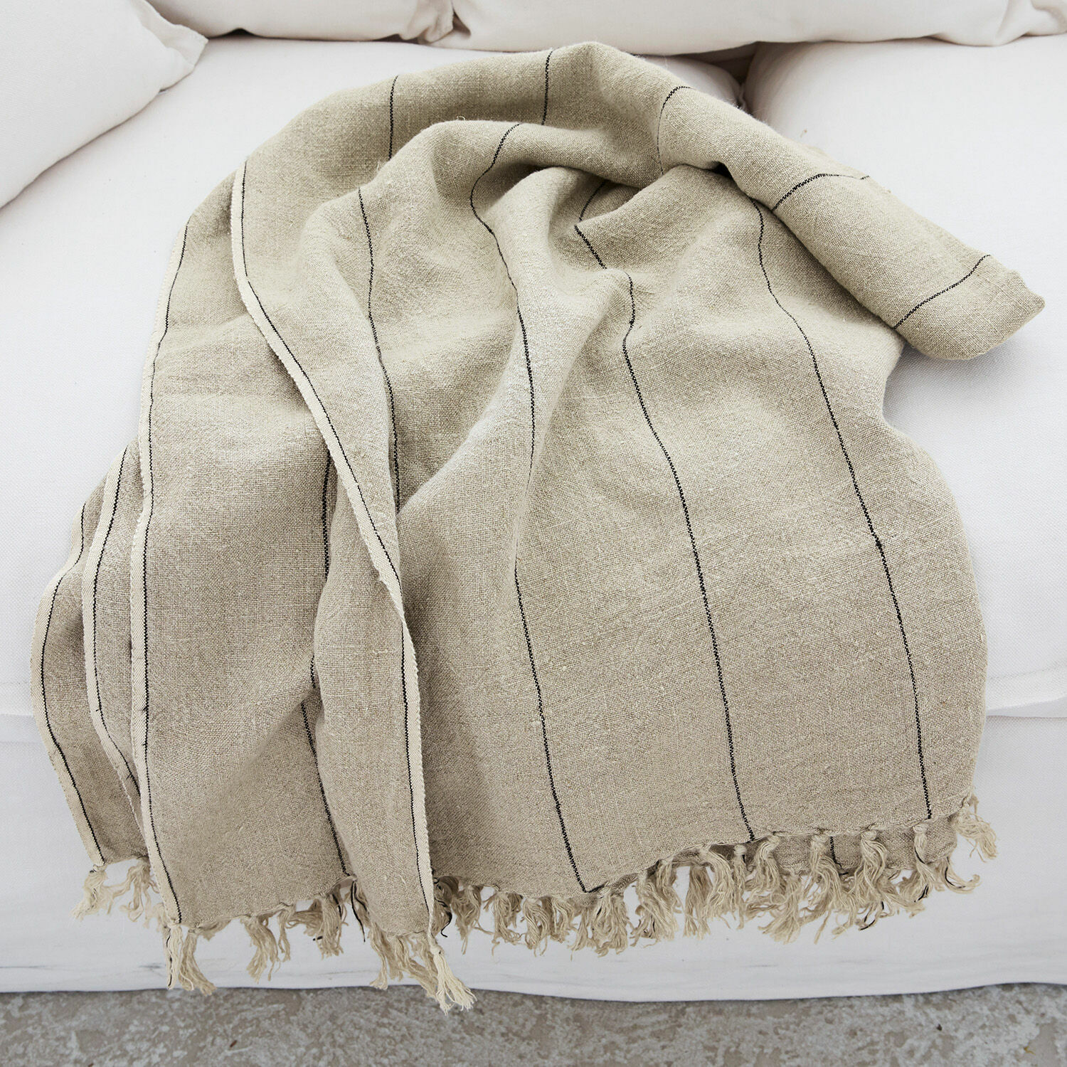 Beige Leinen-Decke mit schwarzen Streifen und Fransen auf weißem Sofa, weich und dekorativ