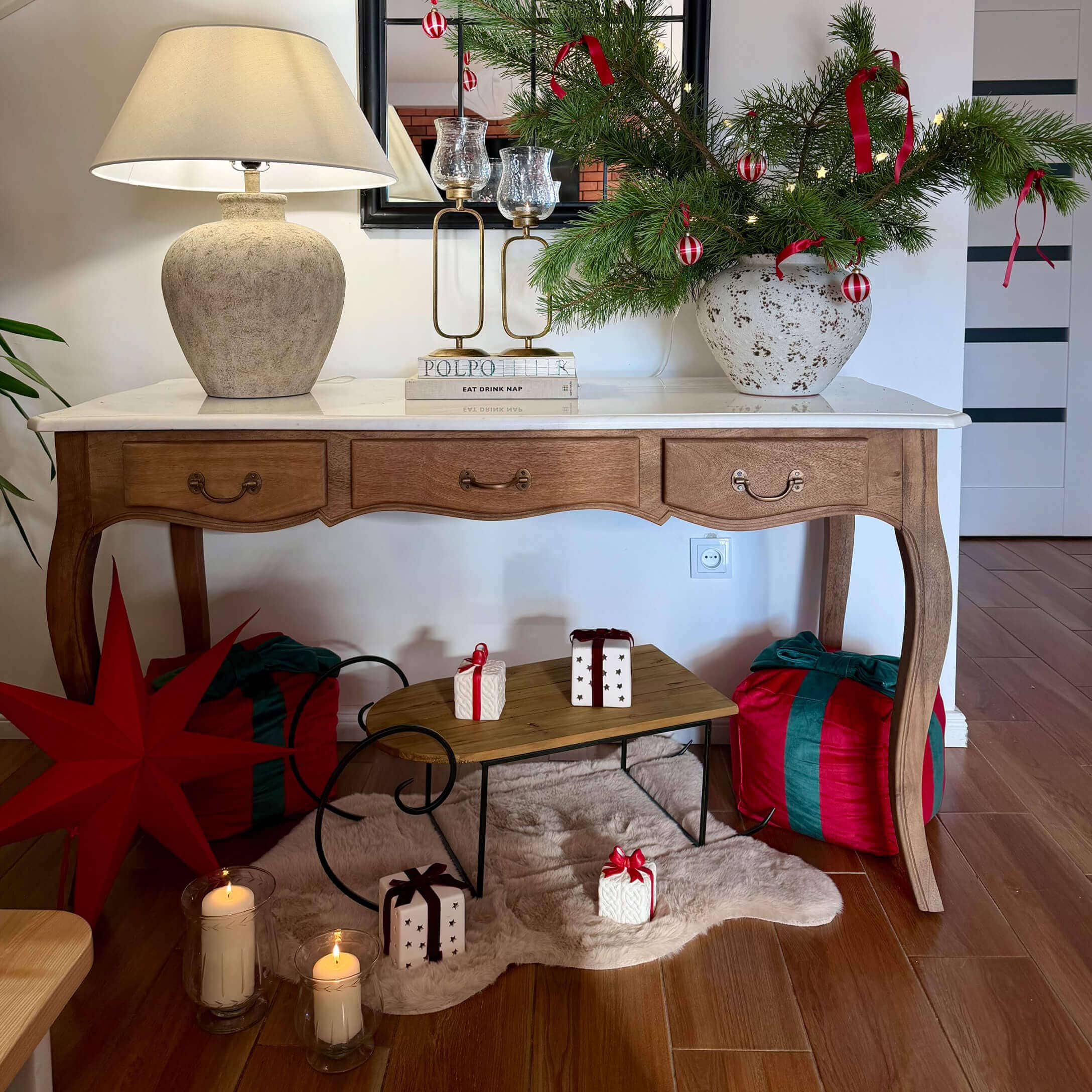 Holztisch mit weißer Platte, Lampe und Weihnachtsdeko aus grünen Zweigen mit roten Bändern