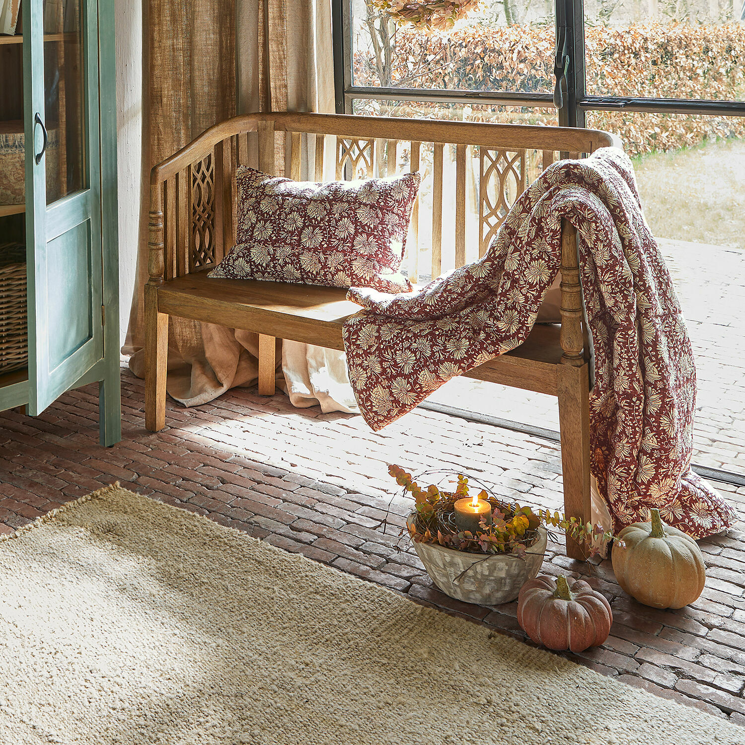 Holzbank mit floral gemustertem bordeauxfarbenem Kissen und Decke, herbstliche Deko mit Kürbissen