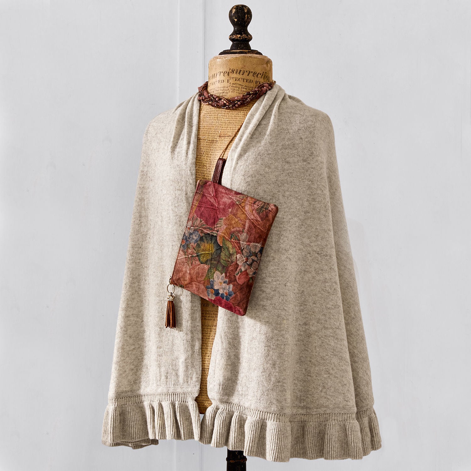 Beiger Wollumhang mit Rüsche am Saum und bunte Blumenmuster-Tasche