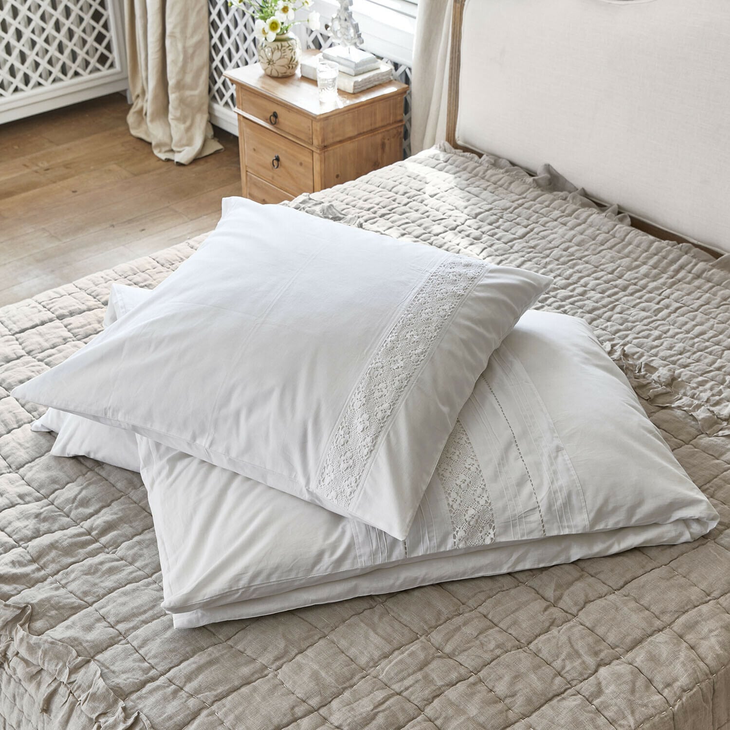 Weiße Baumwoll-Kissenbezüge mit Spitzenverzierung auf beiger Steppdecke im Schlafzimmer