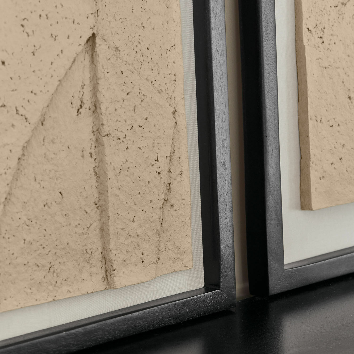 Nahaufnahme eines schwarzen Holzrahmens mit beiger, strukturierter Dekorplatte aus Material.
