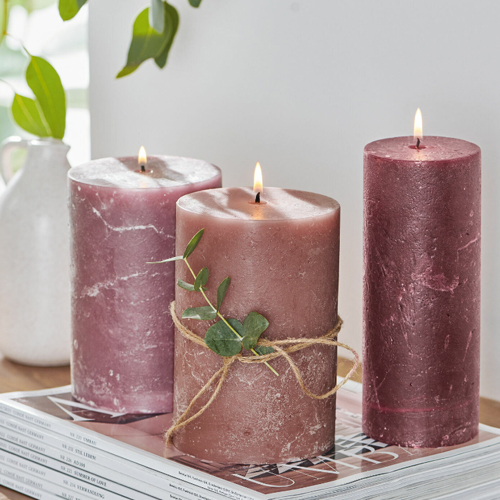 Drei rosa Wachskerzen mit grünen Blättern auf einem Stapel Zeitschriften als Tischdekoration